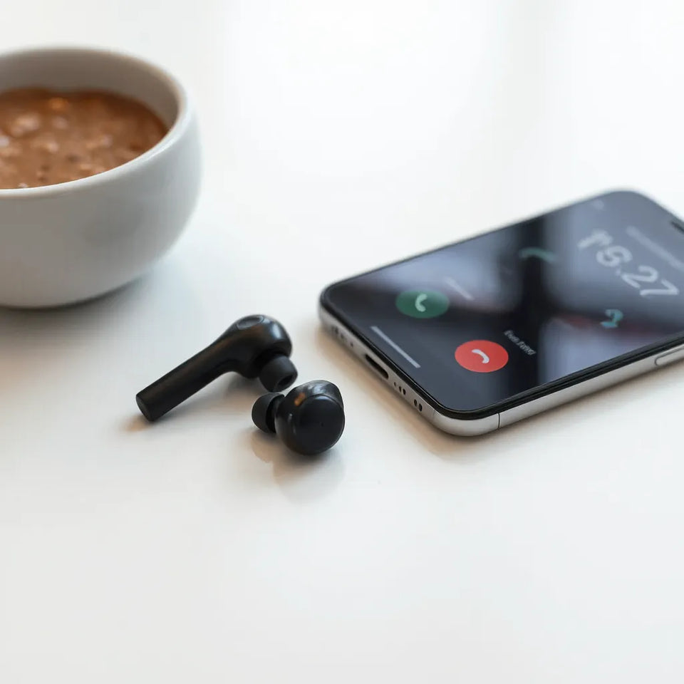 Bluetooth earbuds beside a smartphone with soft call-screen glow, set on a clean surface.